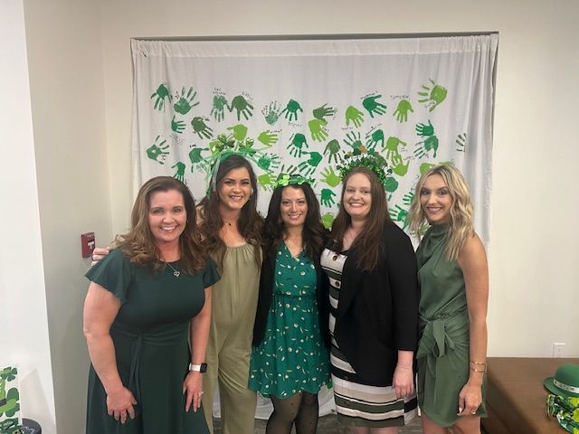A group of women, mostly in green dresses, are posing for a picture.