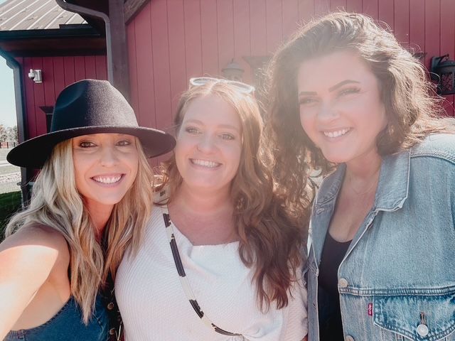 Three women are posing for a picture in front of a red building.