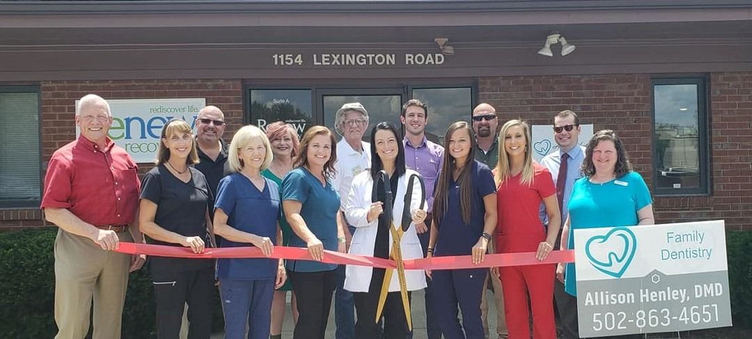 A group of people are standing in front of a building holding a red ribbon.