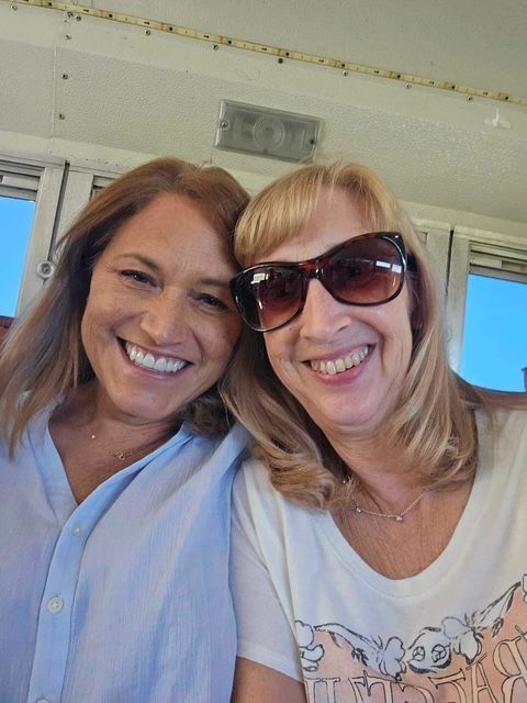 Two women, one wearing sunglasses, are posing together for a photograph.