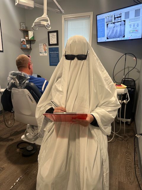 A person dressed as a ghost is holding a clipboard in a dental office.