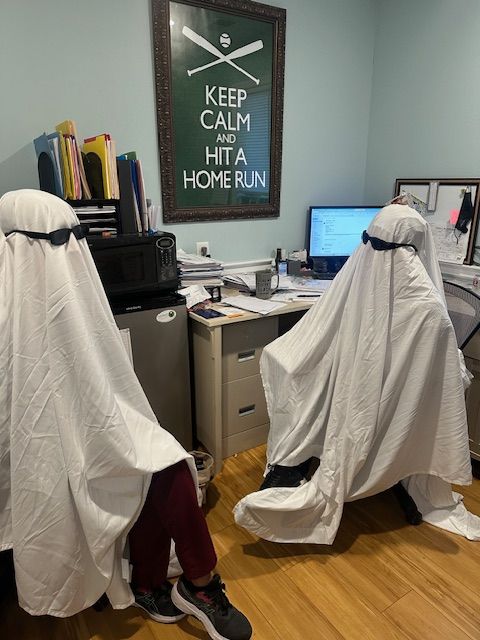 Two people dressed in ghost costumes are seated in an office setting.
