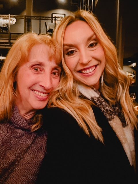 Two smiling women pose close together indoors.