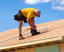 Construction worker using nail gun to nail osb sheeting on roof of a new home