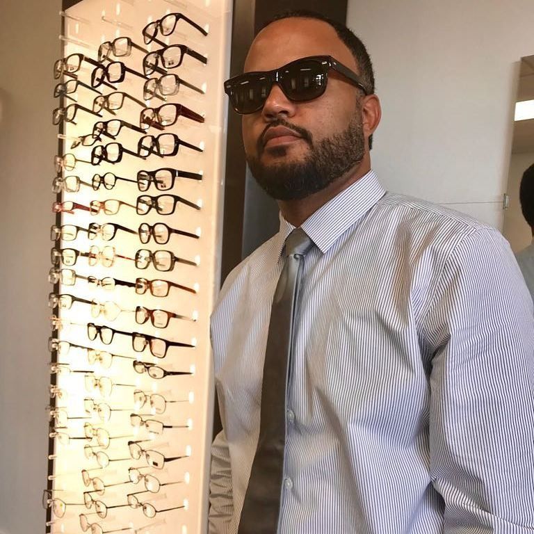 A man wearing sunglasses stands in front of a display of glasses