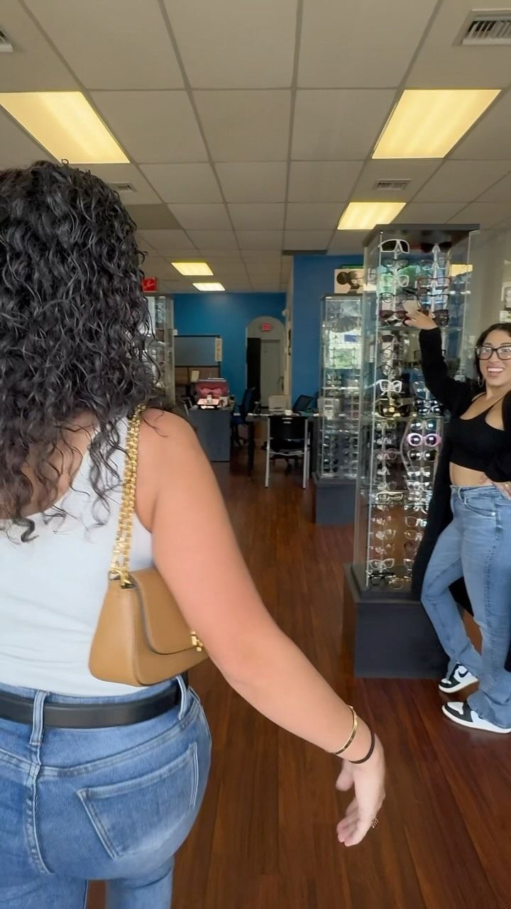 A woman in a white tank top and blue jeans is standing in a store.