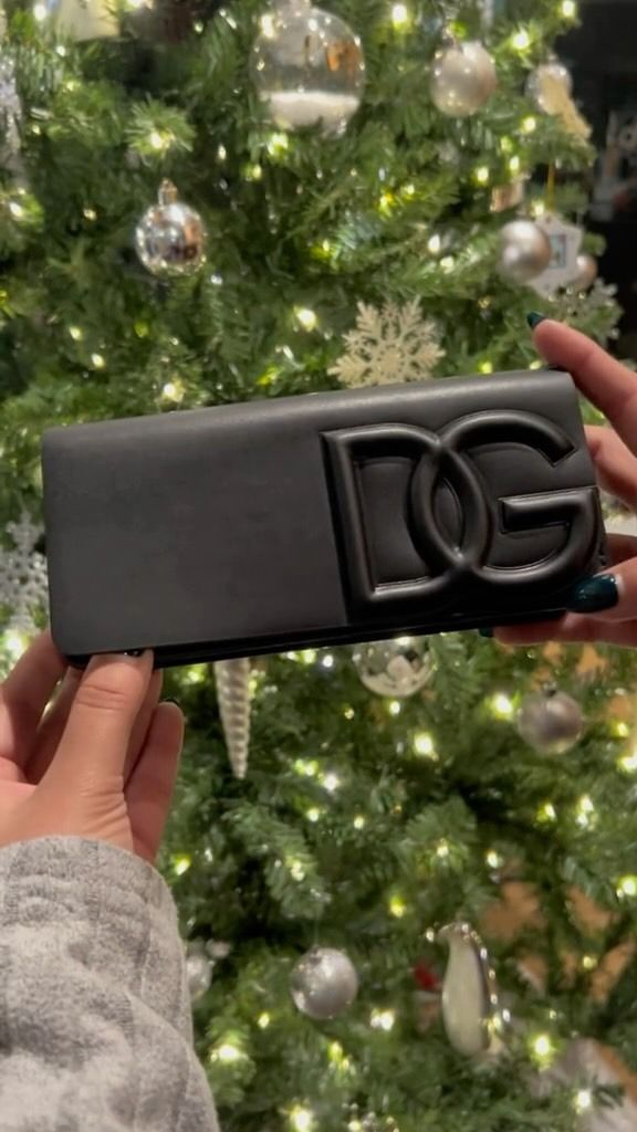 A person is holding a black wallet in front of a christmas tree.