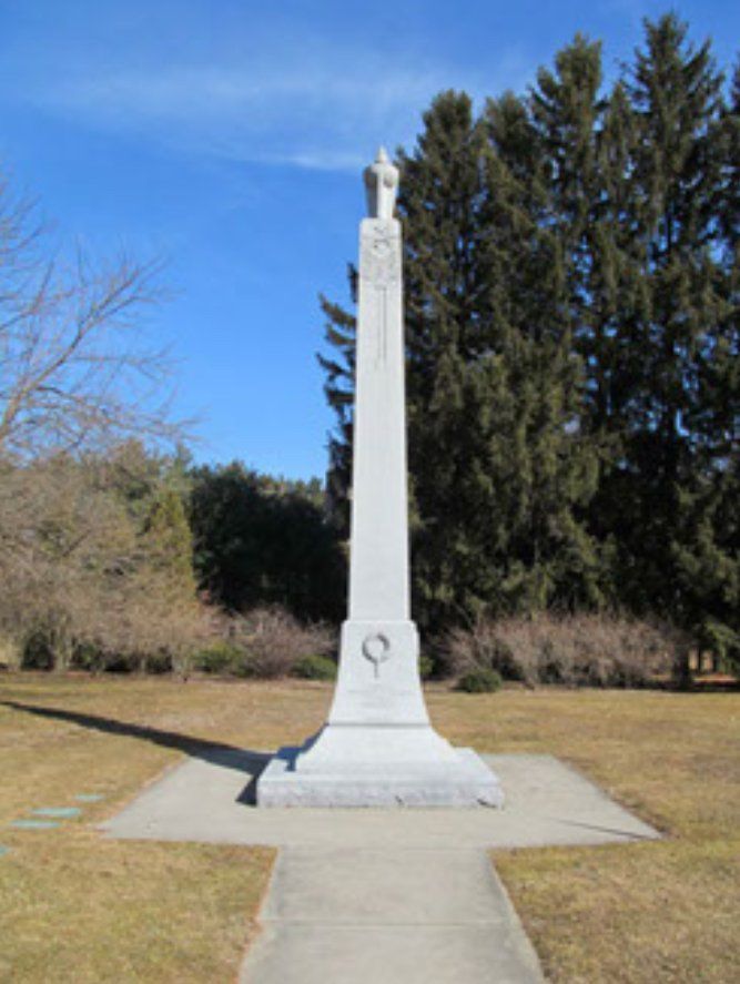 A large white obelisk in a park with trees in the background