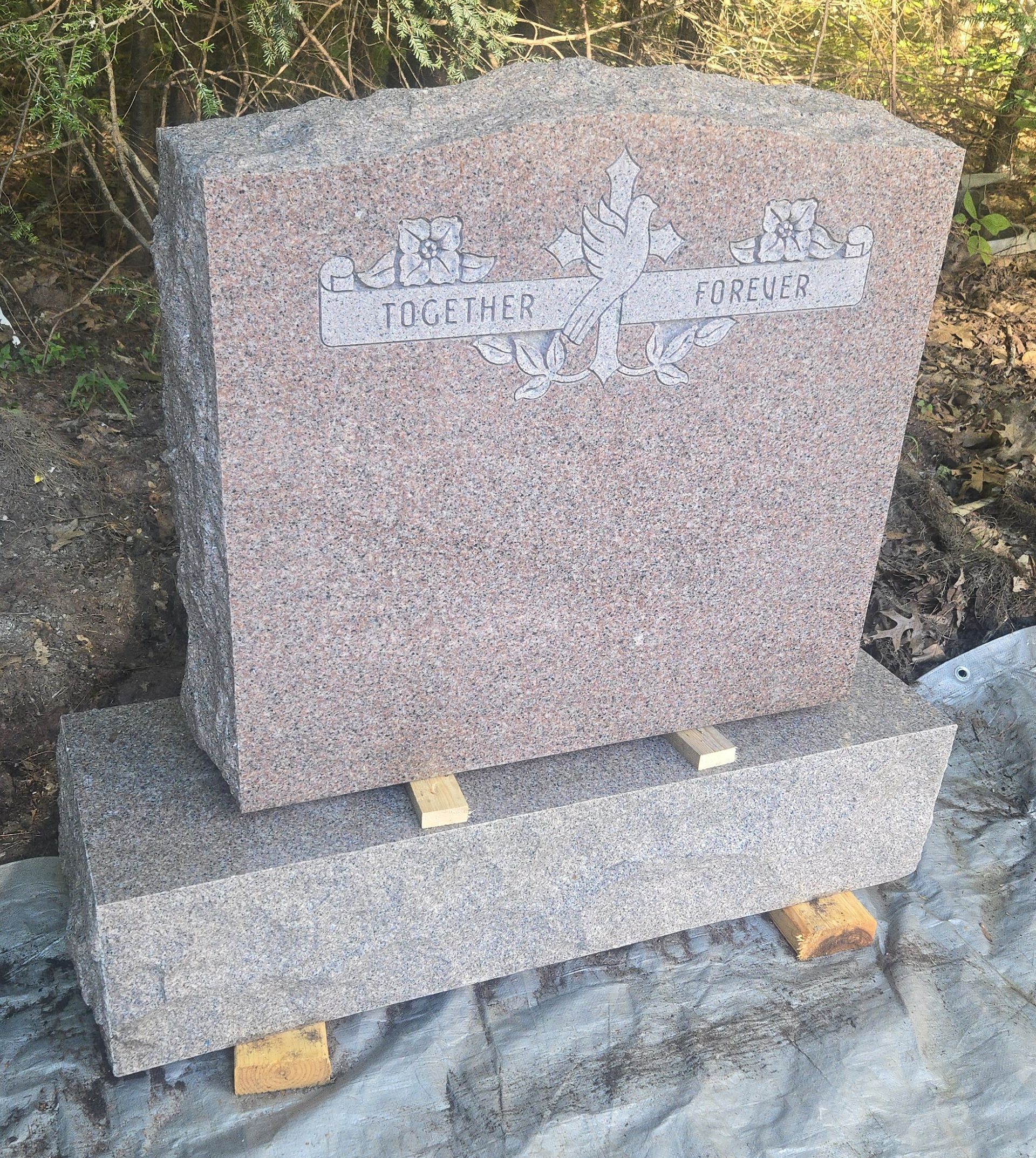 Granite gravestone on a matching base in an outdoor wooded area