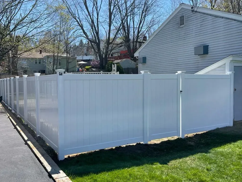 White vinyl privacy fence enclosing a grassy yard beside a white house on a sunny day.
