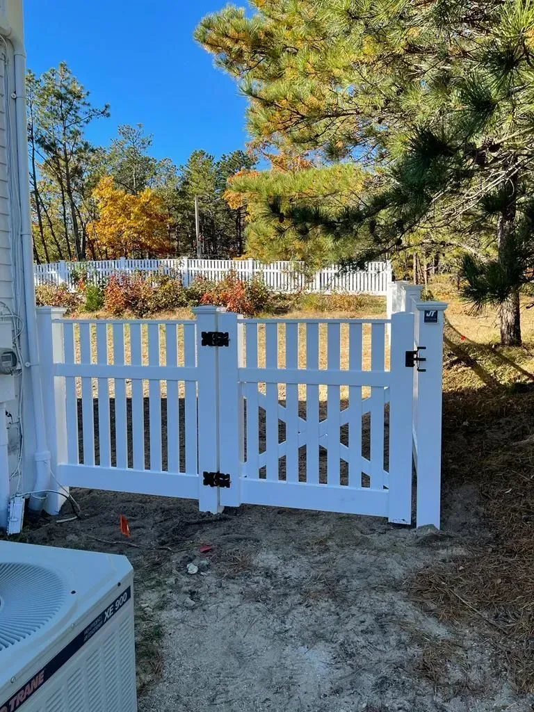 White wooden gate at a driveway entrance with trees and a house in the background.