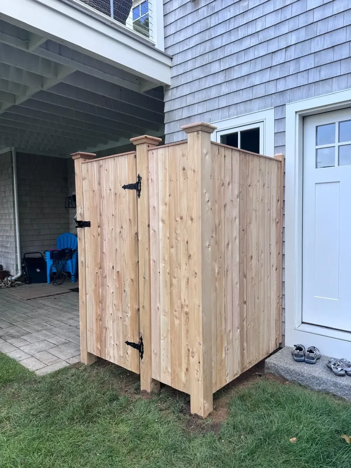 Wooden outdoor enclosure beside a house, with a white door and covered patio nearby.