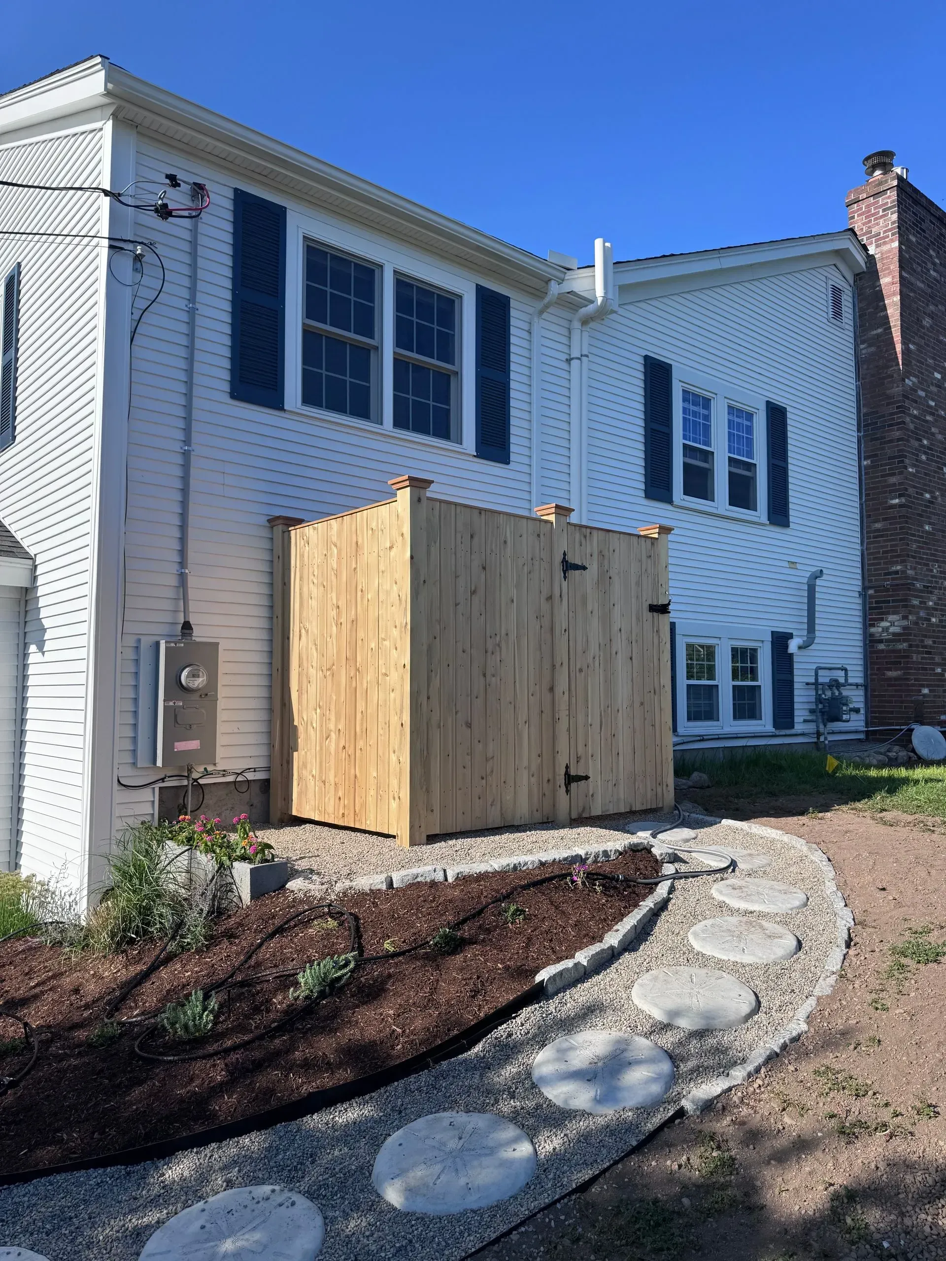 White two-story house with a wooden utility enclosure and a curved stone garden path in front.