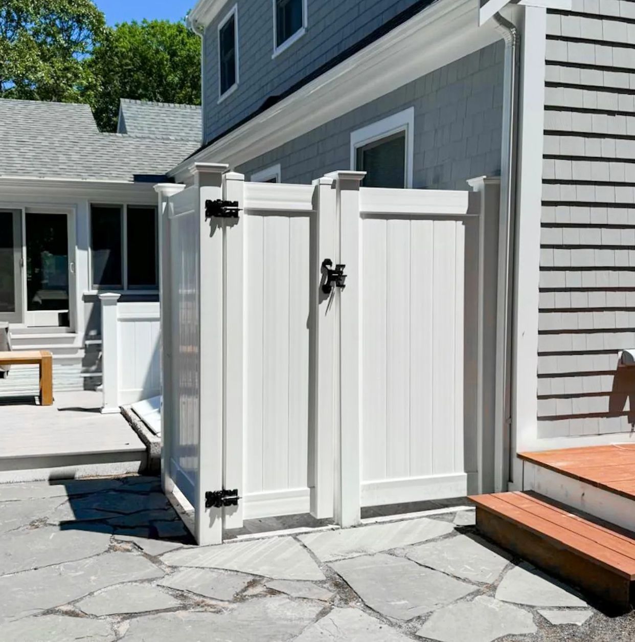 White vinyl gate beside a gray house on a stone patio, with a small deck step nearby.