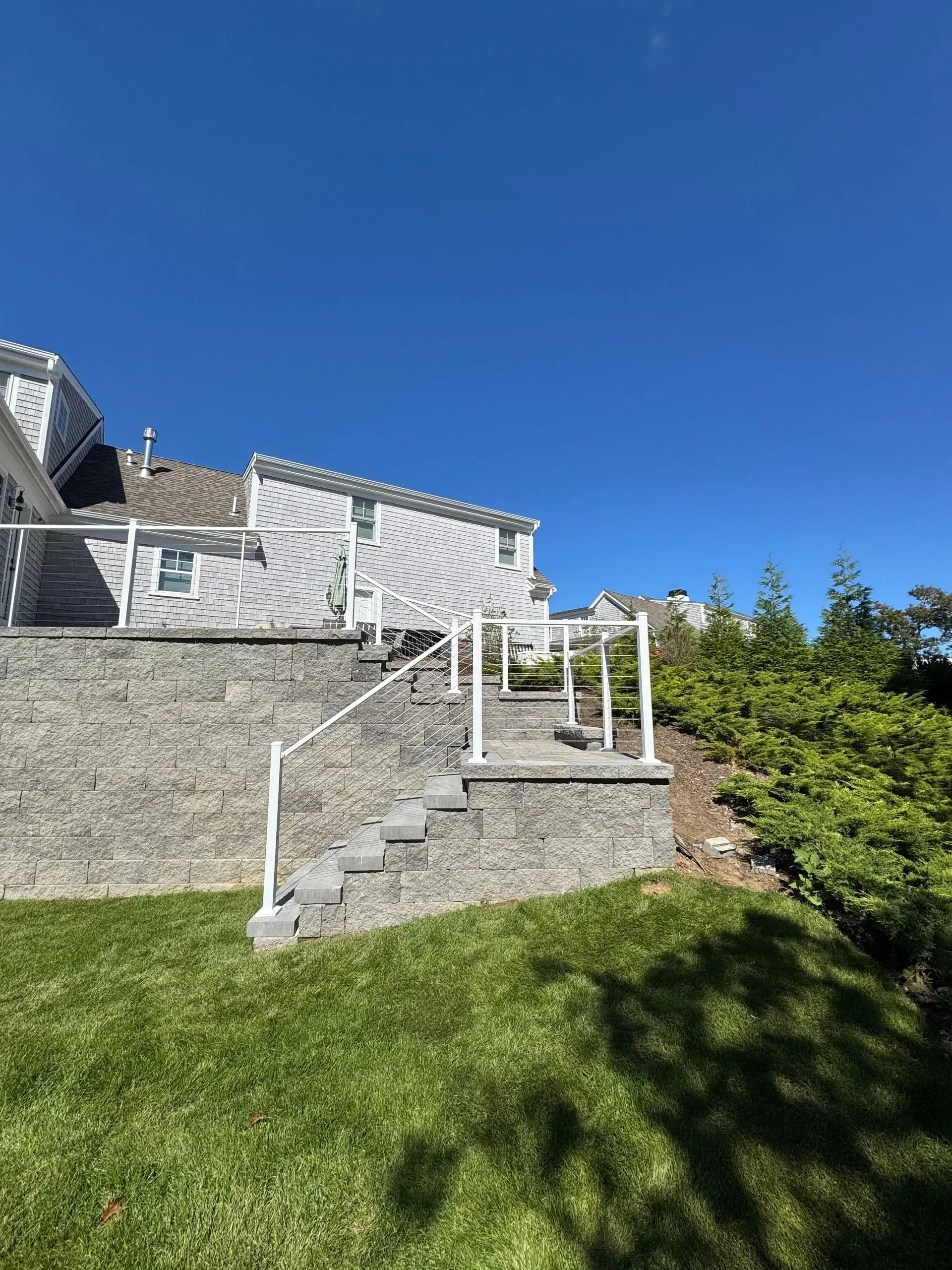 Stone steps and white railing leading to a deck beside a house under a clear blue sky.