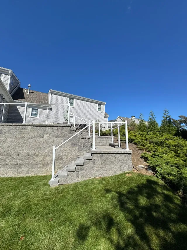 Stone steps and white railing leading to a deck beside a house under a clear blue sky.