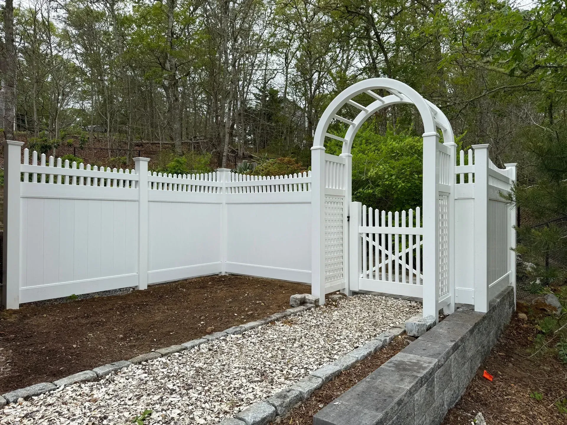 White arched garden gate and fence with gravel path in a landscaped yard.