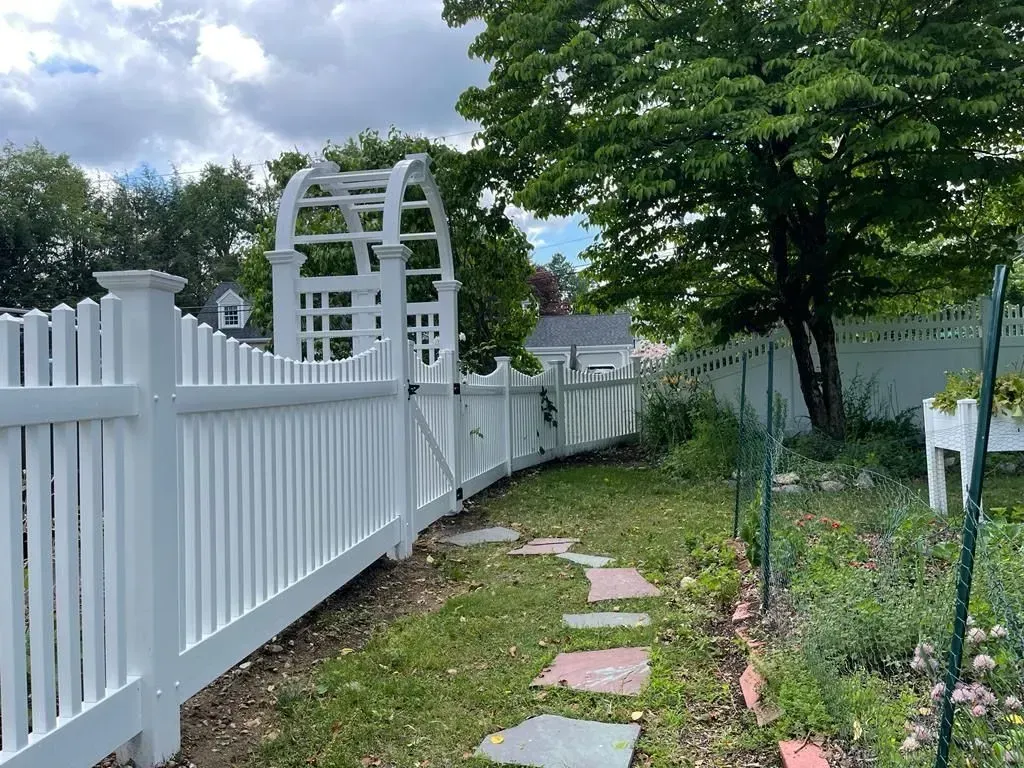 White picket fence beside a stone path and garden arch in a green backyard.