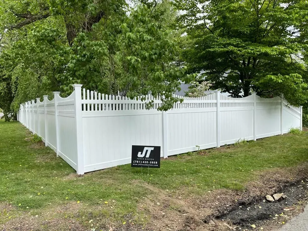 White vinyl fence enclosing a yard beneath trees, with a small black sign in front.