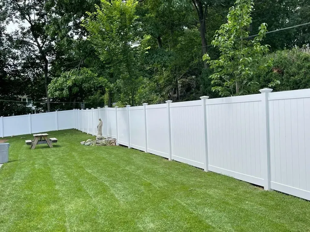 Grassy backyard with a white fence and trees along the border.