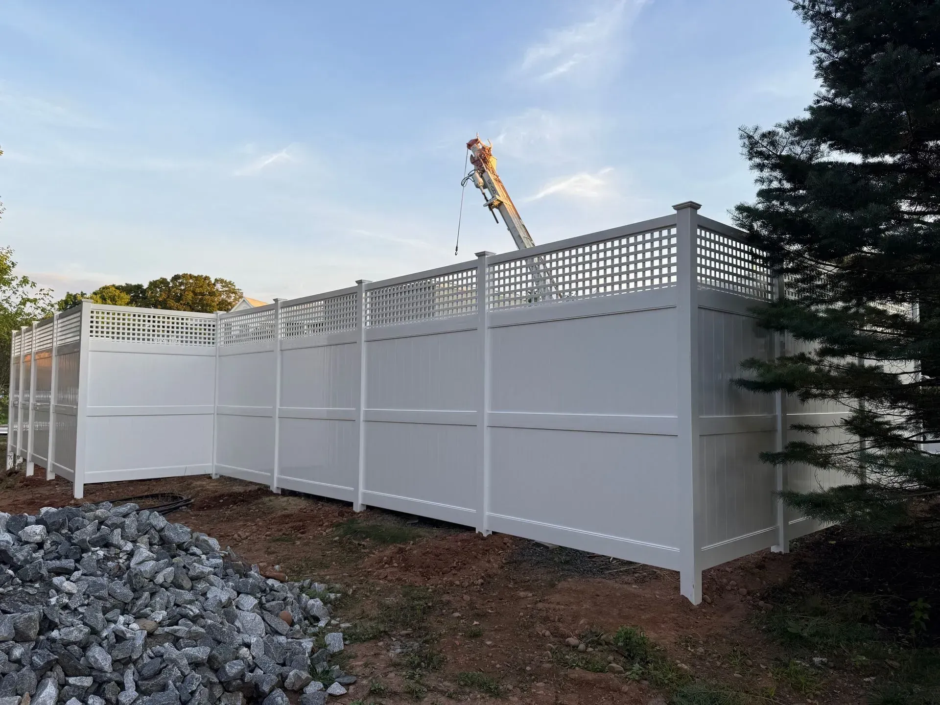 White privacy fence around a yard, with construction equipment visible behind it at dusk.