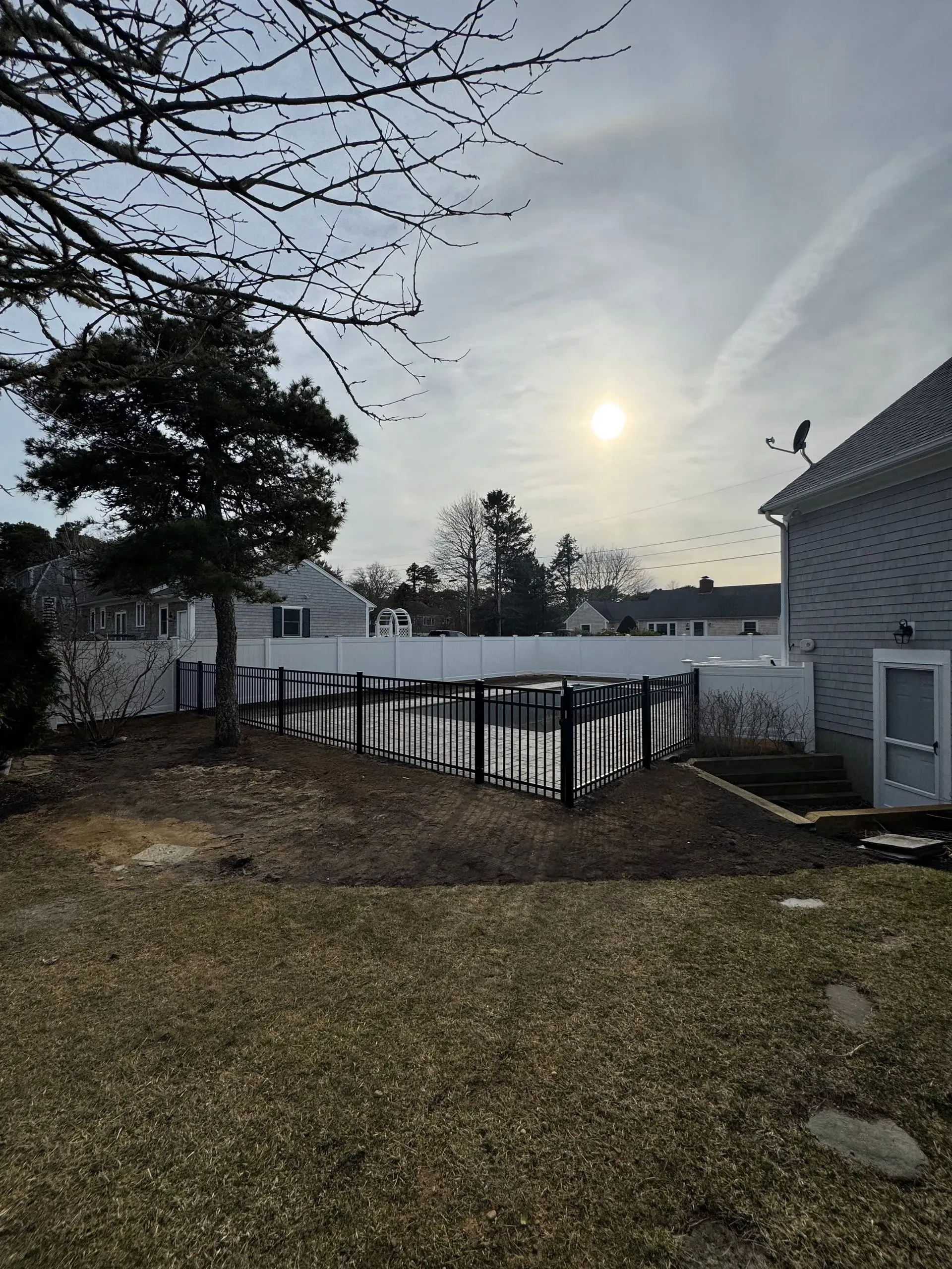 Backyard with bare trees, a fence, and a small pond under a bright low sun.