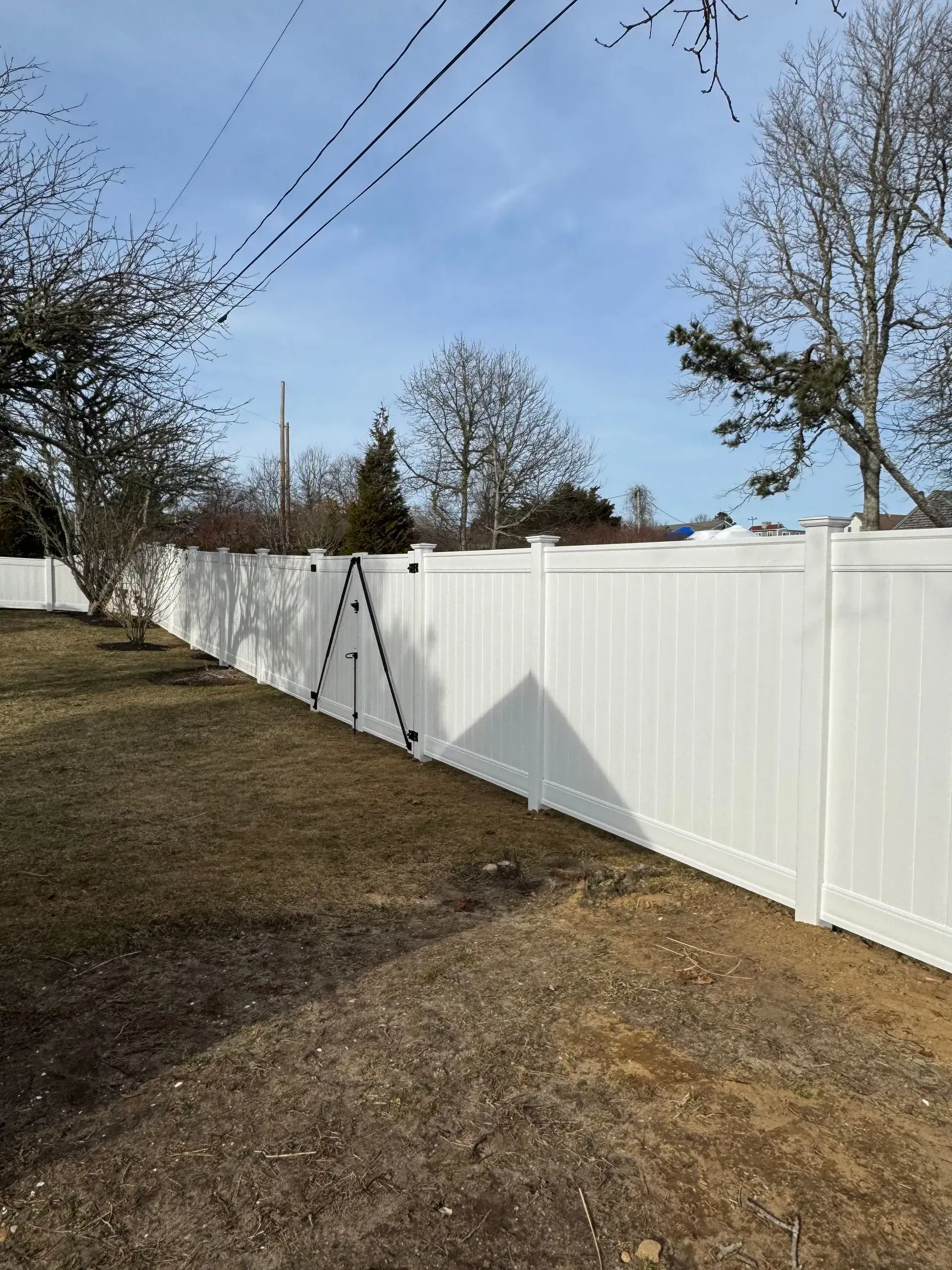 White vinyl fence along a grassy yard under a blue sky with power lines overhead.