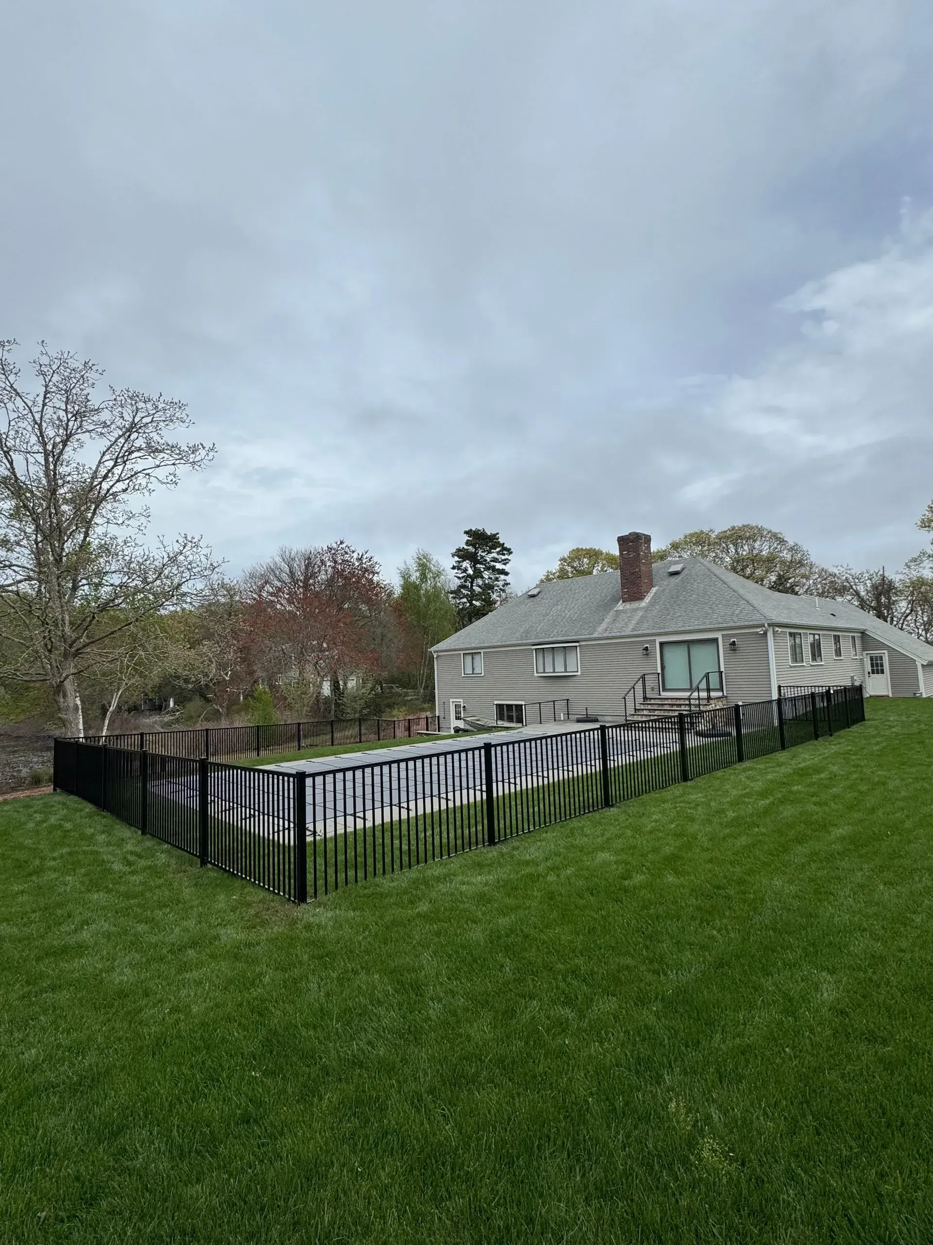 House with fenced yard on a grassy hill under a cloudy sky.