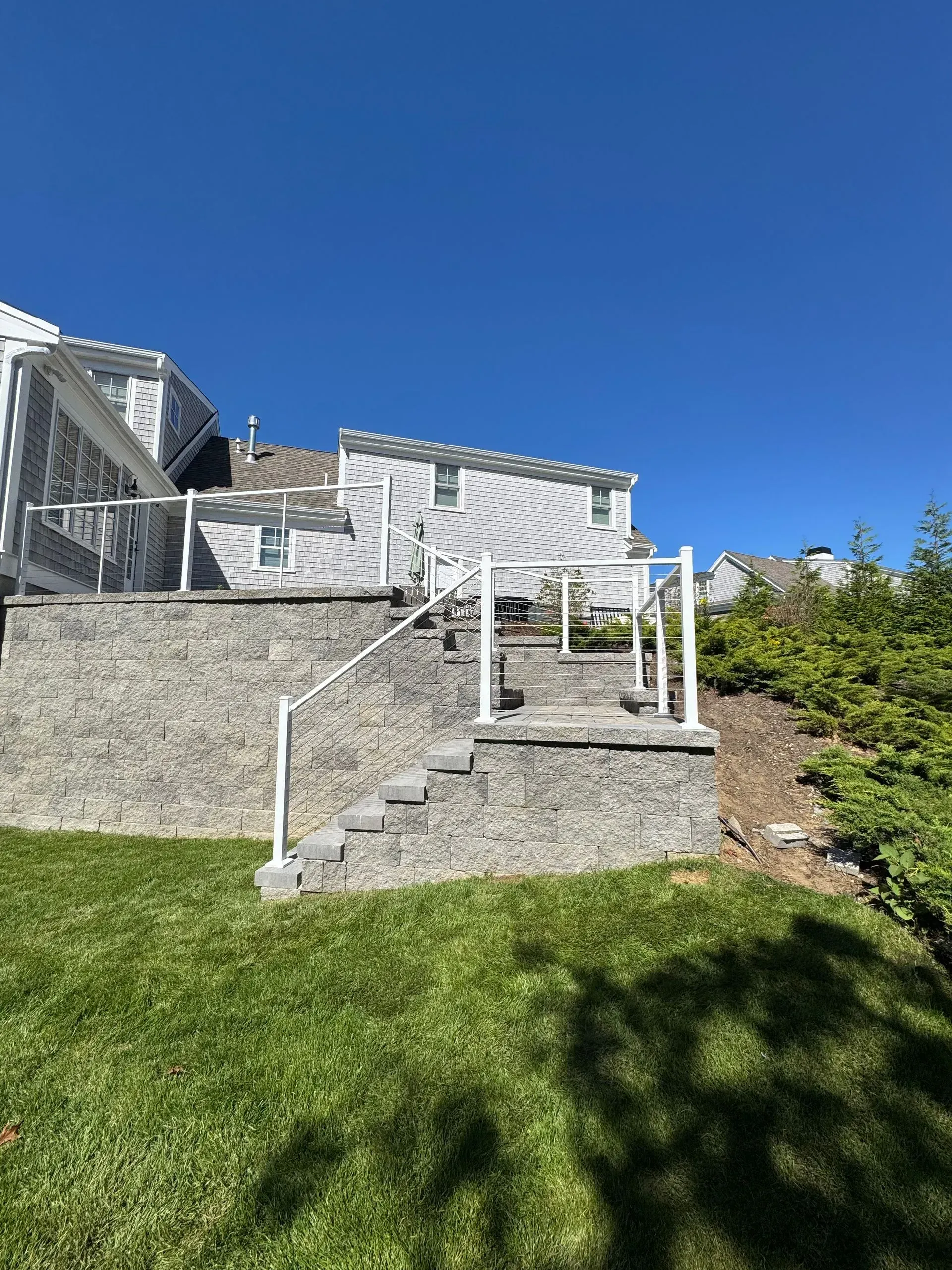 Stone stairs leading to a white deck on a grassy hillside under a clear blue sky.