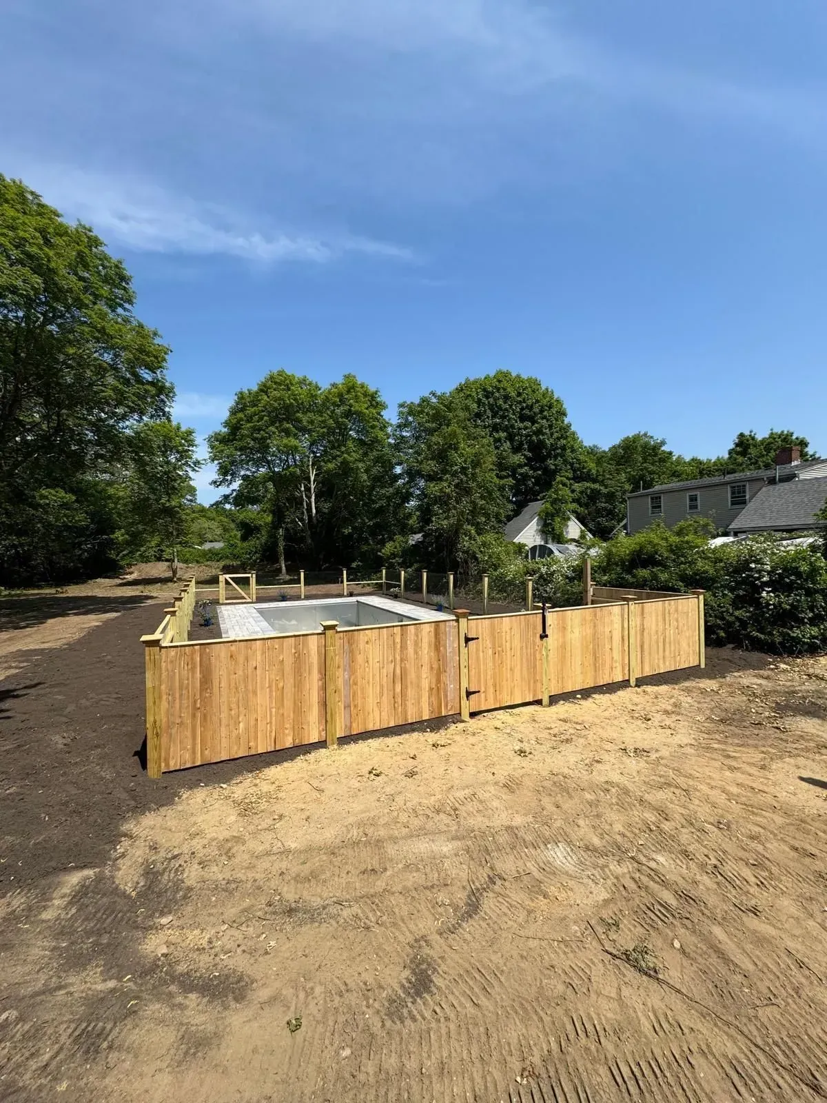 Partially built wooden fence around a concrete foundation on a dirt lot under a clear blue sky.