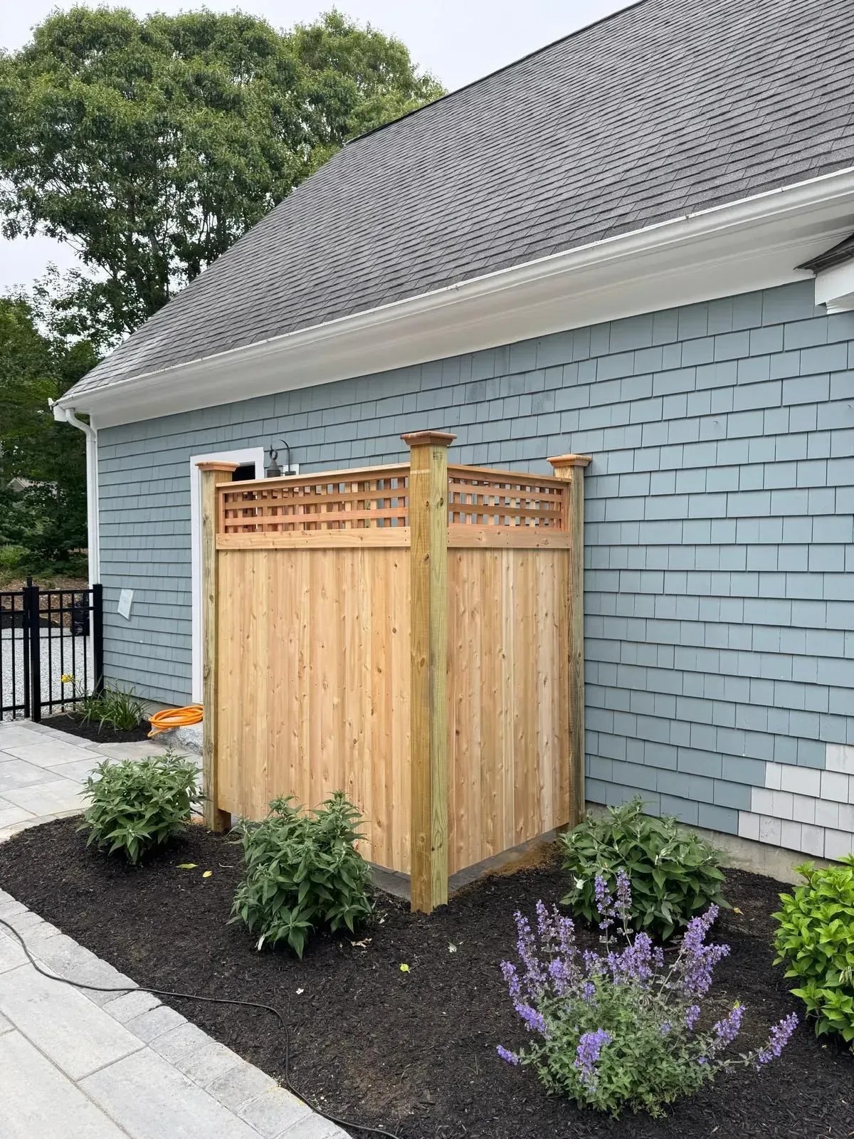 Wooden privacy screen beside a light blue house, surrounded by fresh mulch and flowers.