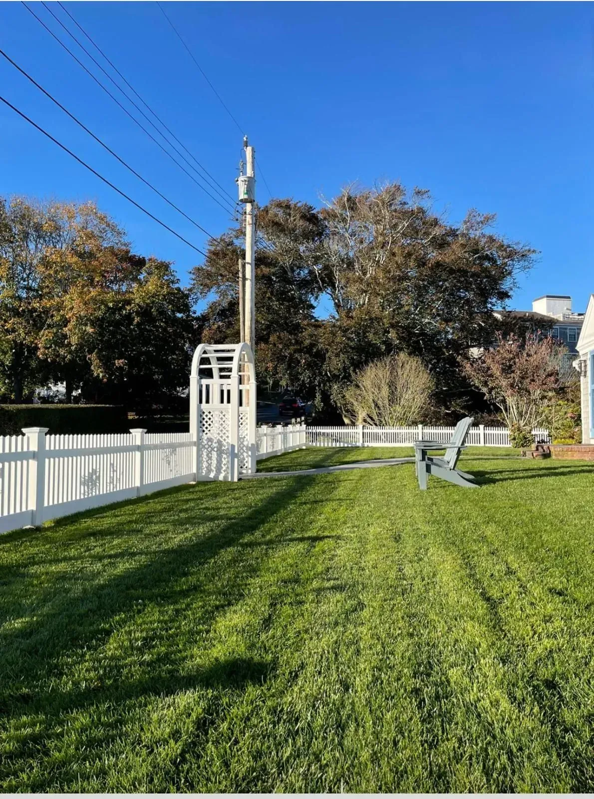 White picket fence lining a grassy field with a tall light pole under a clear blue sky.