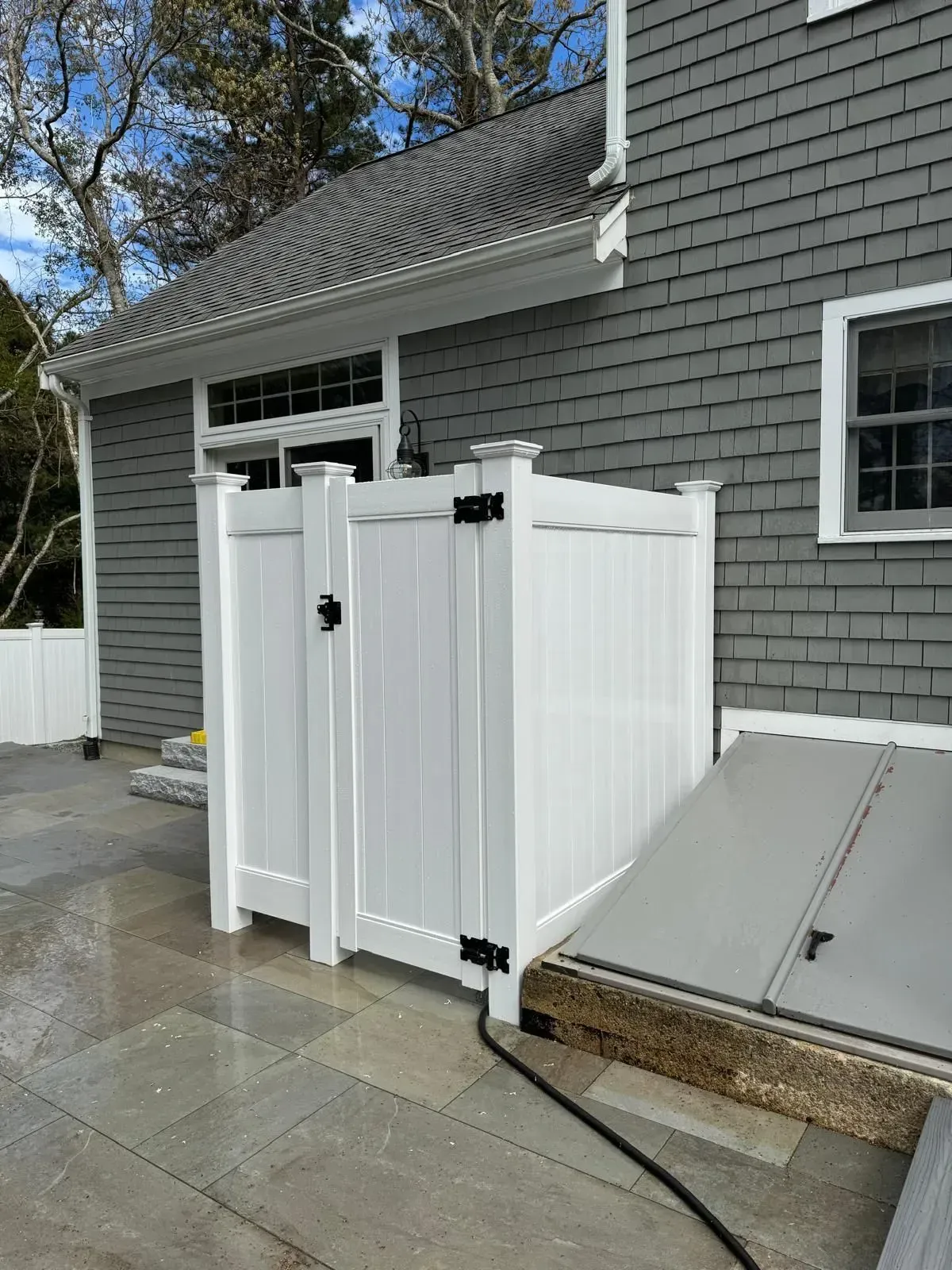 White plastic gate panels beside a gray house and concrete patio.