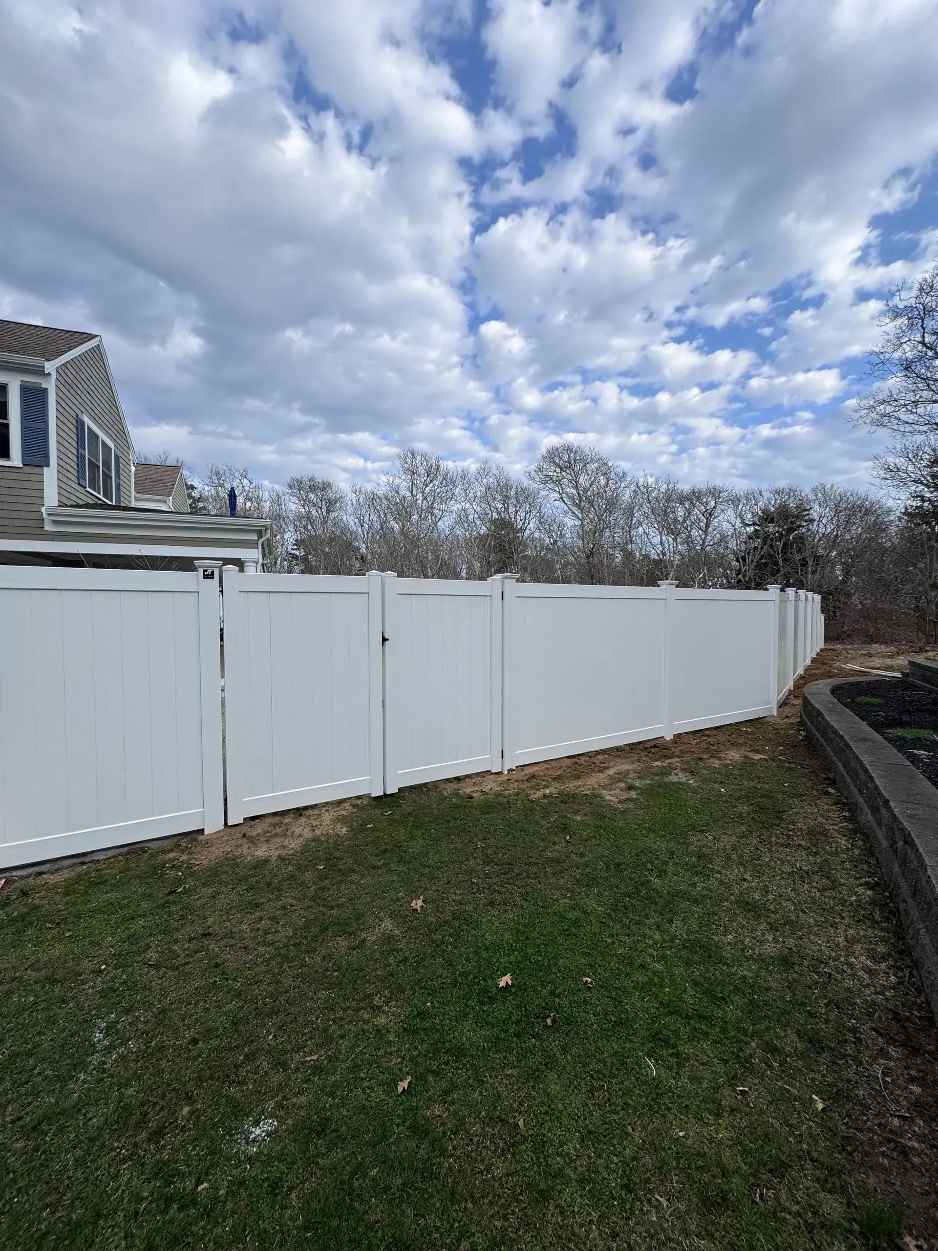 White vinyl fence beside a grassy yard under a cloudy sky.