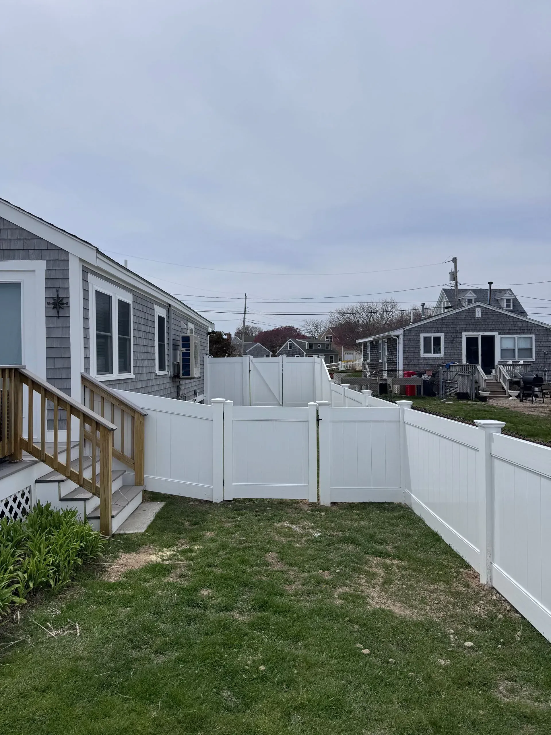 Backyard with white vinyl fence, small house deck, and cloudy sky.