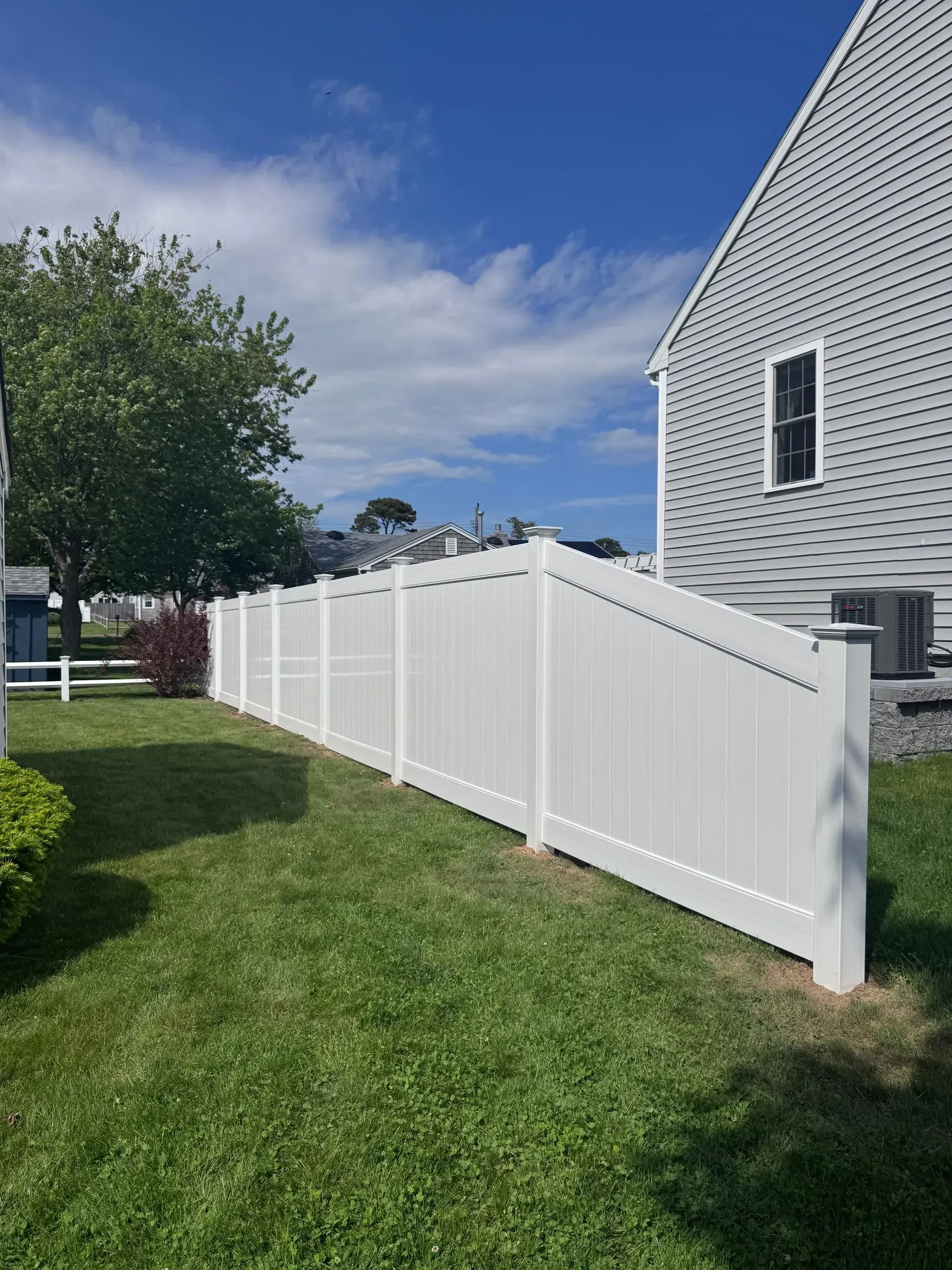 White vinyl fence along a grassy yard beside a house under a blue sky.