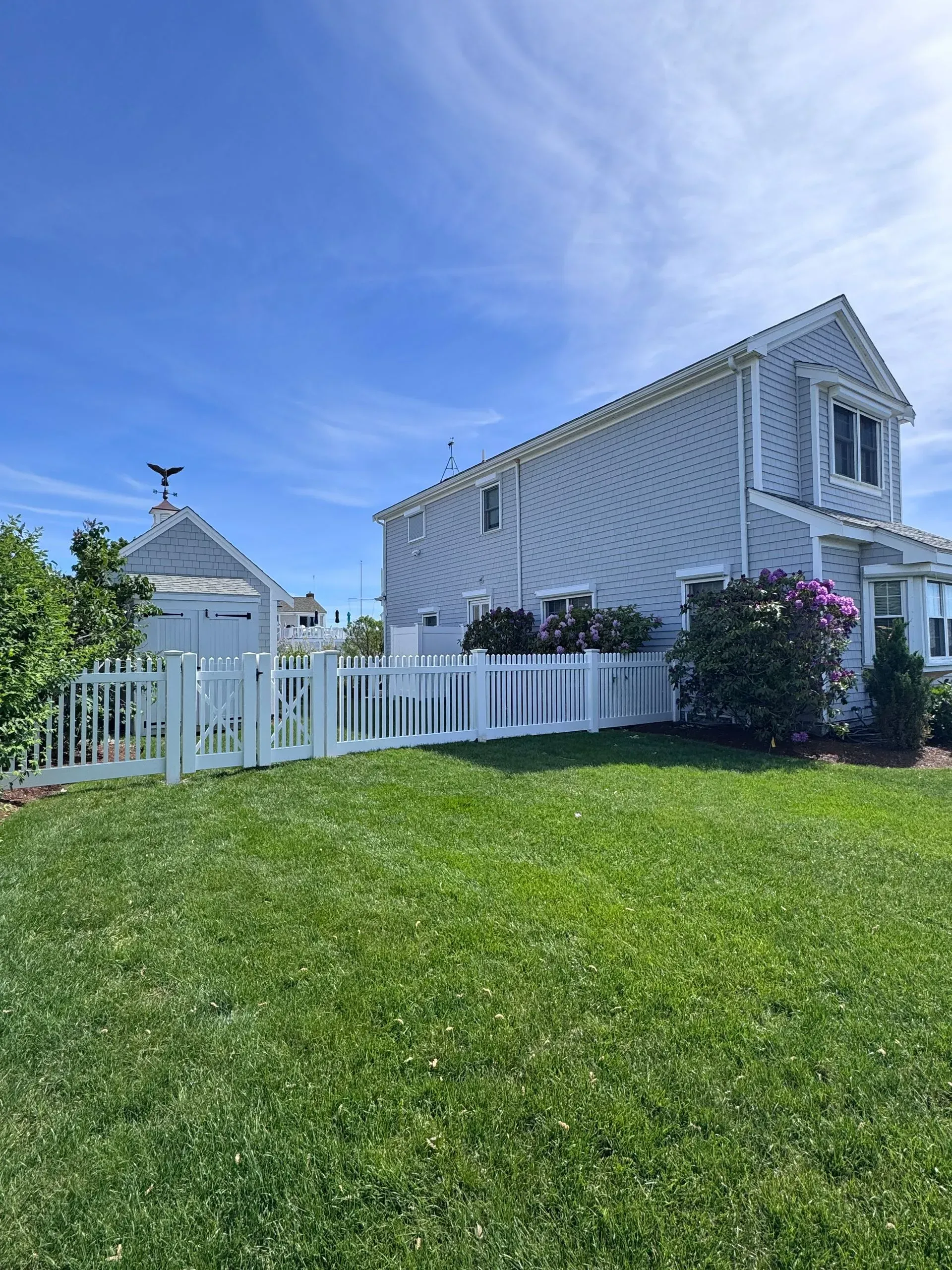 White seaside house with picket fence and green lawn under a bright blue sky.