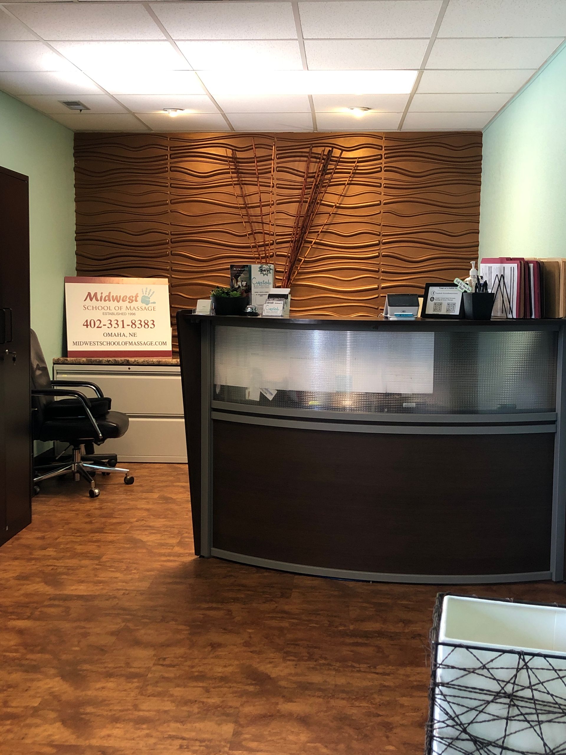 Reception desk in a small office with wood flooring, textured wood wall, and chairs on the left.