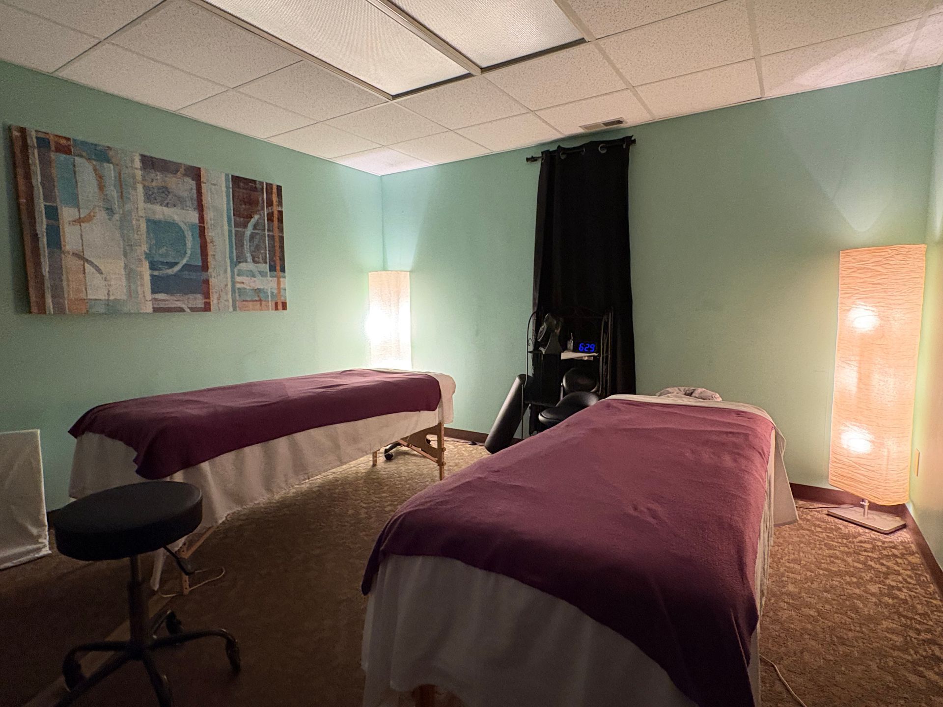 Massage room with two treatment tables, teal walls, warm lamps, and a stool.