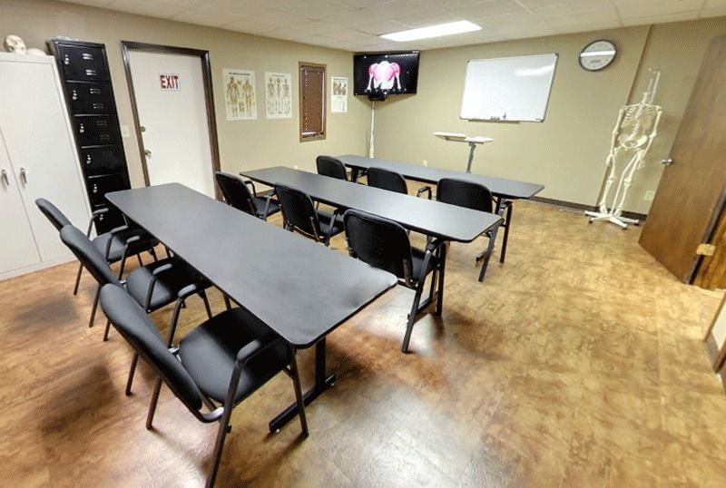 Empty meeting room with black tables and chairs, wall-mounted TV, whiteboard, and wood flooring