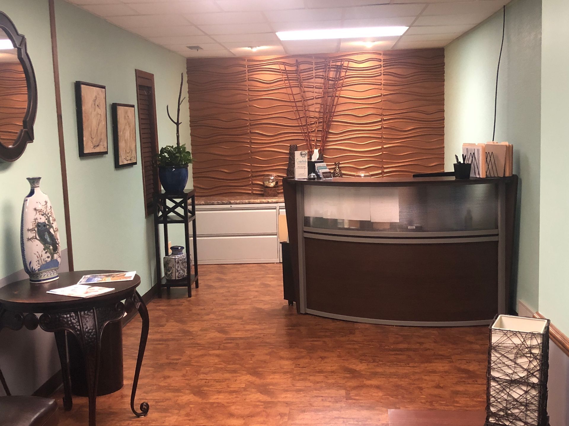 Empty reception area with wood floor, green walls, a curved front desk, and a brick accent wall.