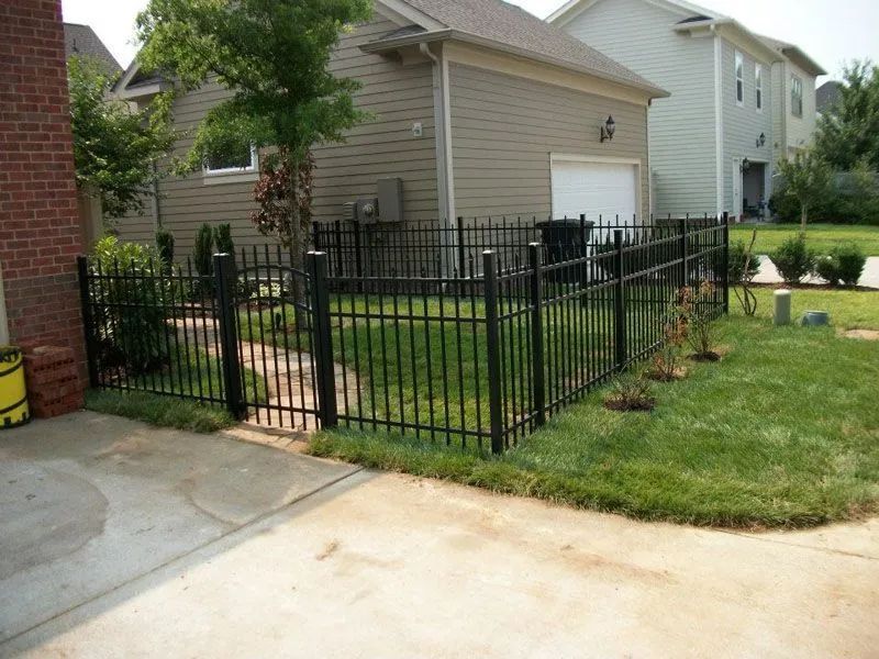Black metal fence surrounding a yard with grass, bushes, and a garage in the background.