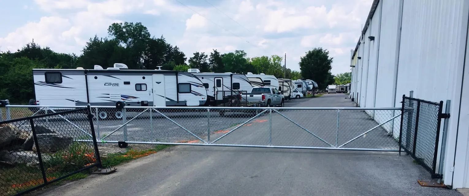 RV storage area with RVs parked behind a chain link gate next to a white building.