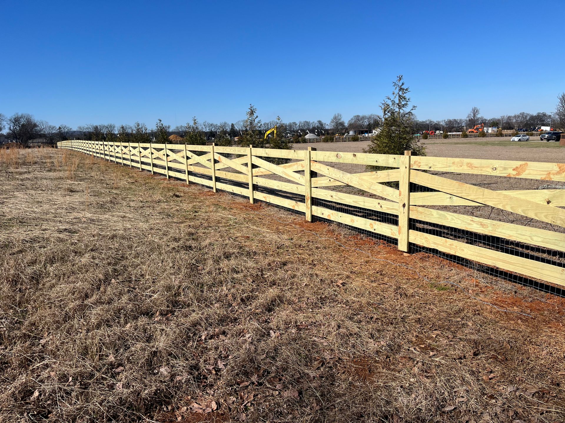 Wooden fence with a zig-zag design stretches across a field under a blue sky.