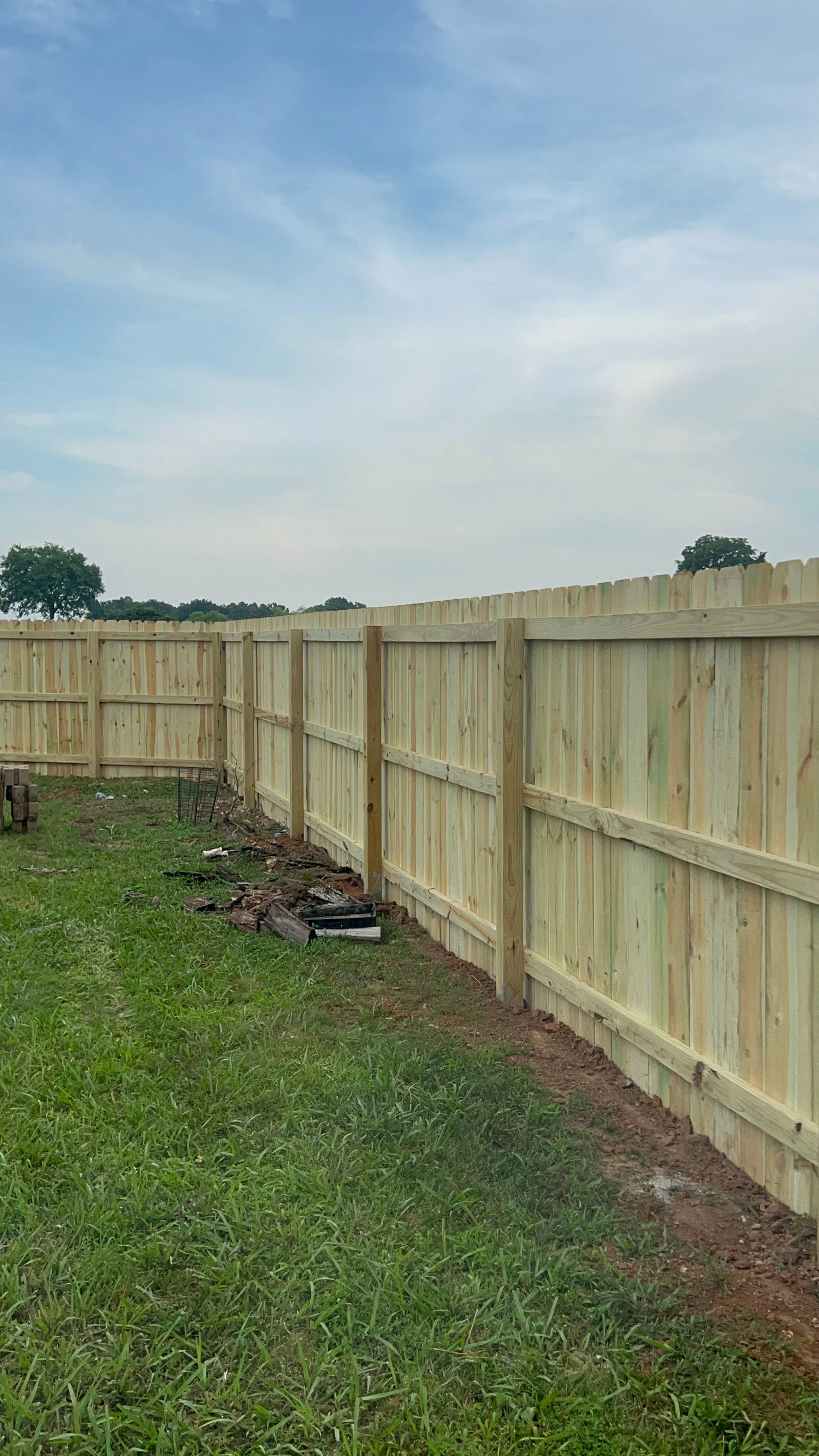 Wooden fence in a yard with green grass and a partly cloudy sky.