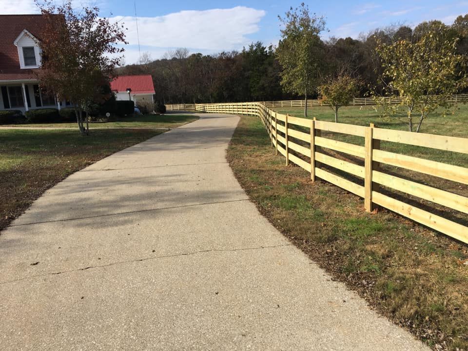A long concrete driveway curves past a wooden fence and a house with a red roof.