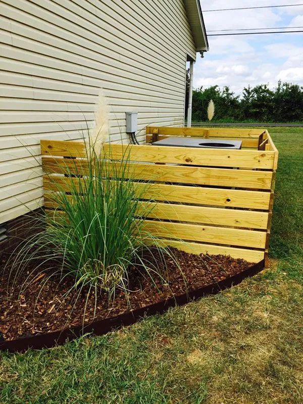 Wooden enclosure around an outdoor AC unit next to a house, with landscaping in front.