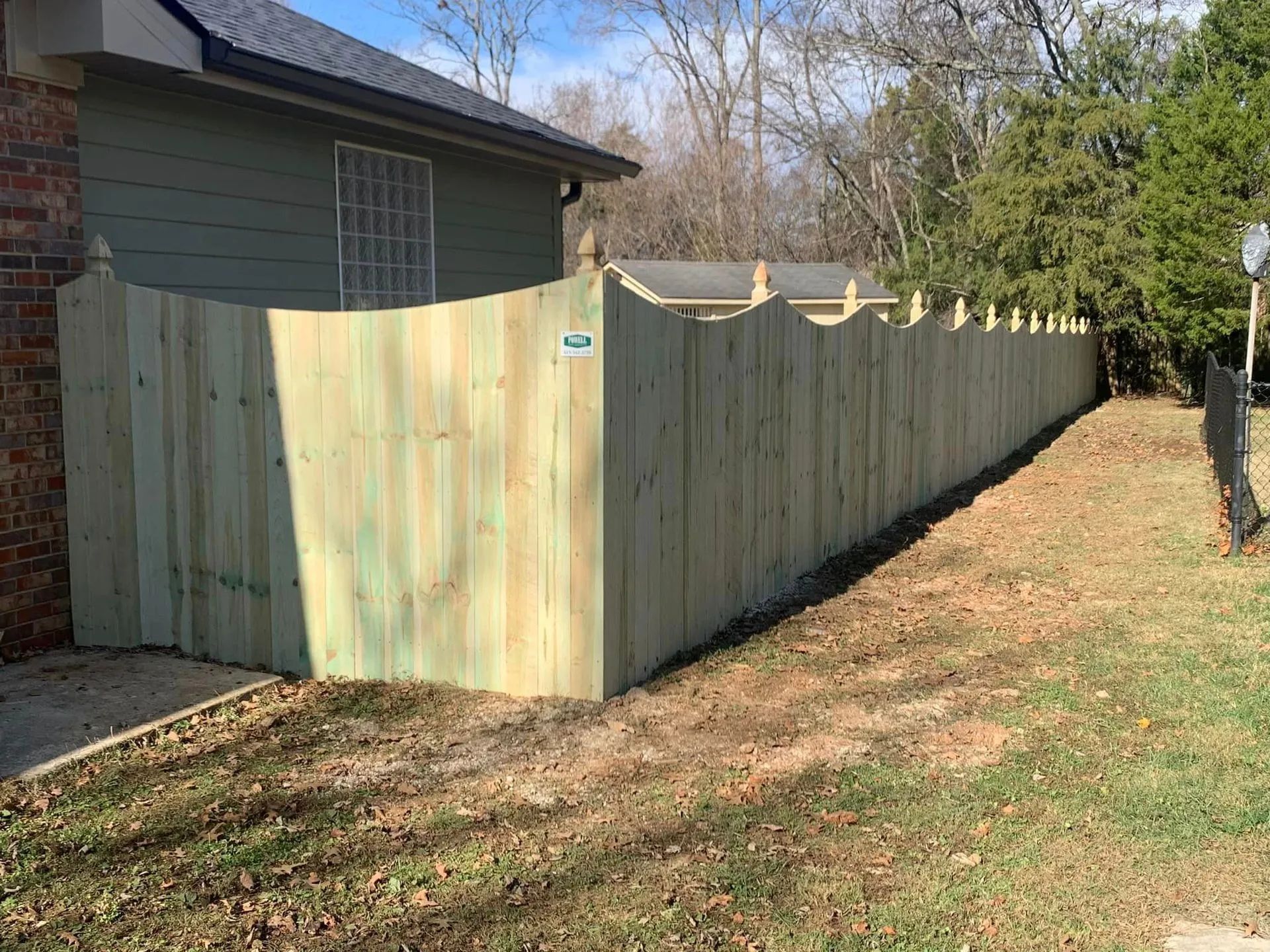 Wooden fence along the side of a green-sided house and yard.