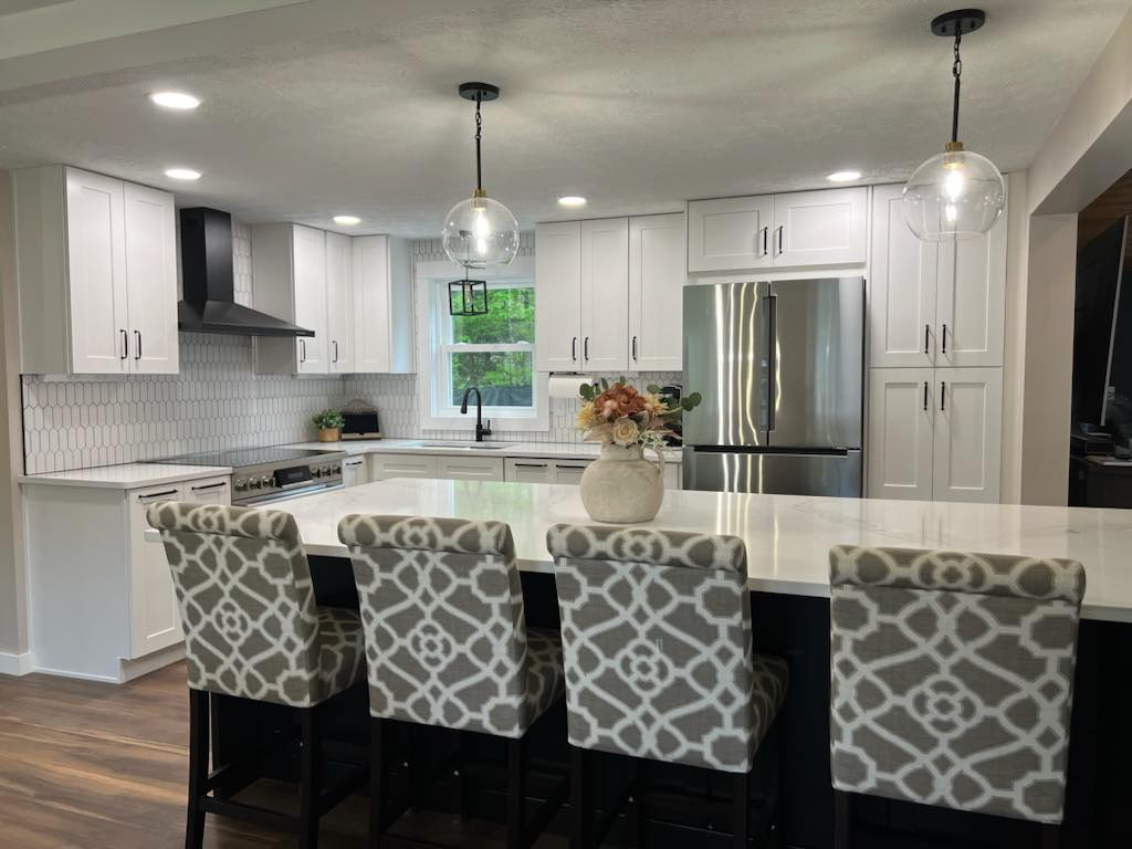 A kitchen with white cabinets , stainless steel appliances , a large island and chairs.