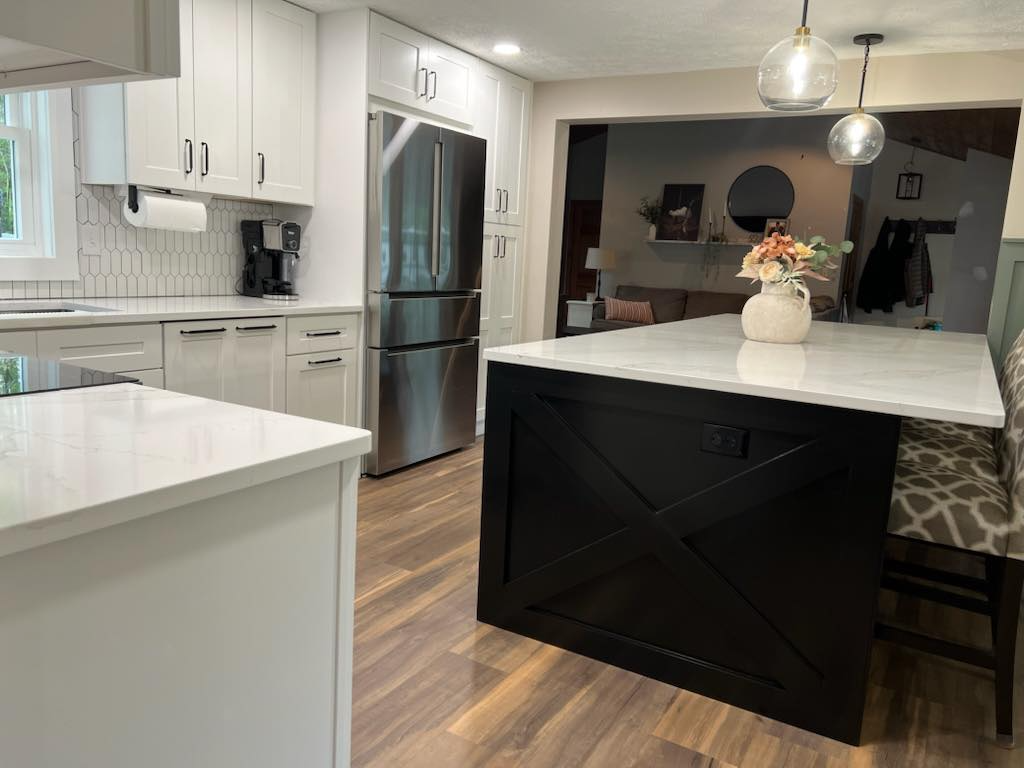 A kitchen with white cabinets , stainless steel appliances , a black island and a vase of flowers on the counter.